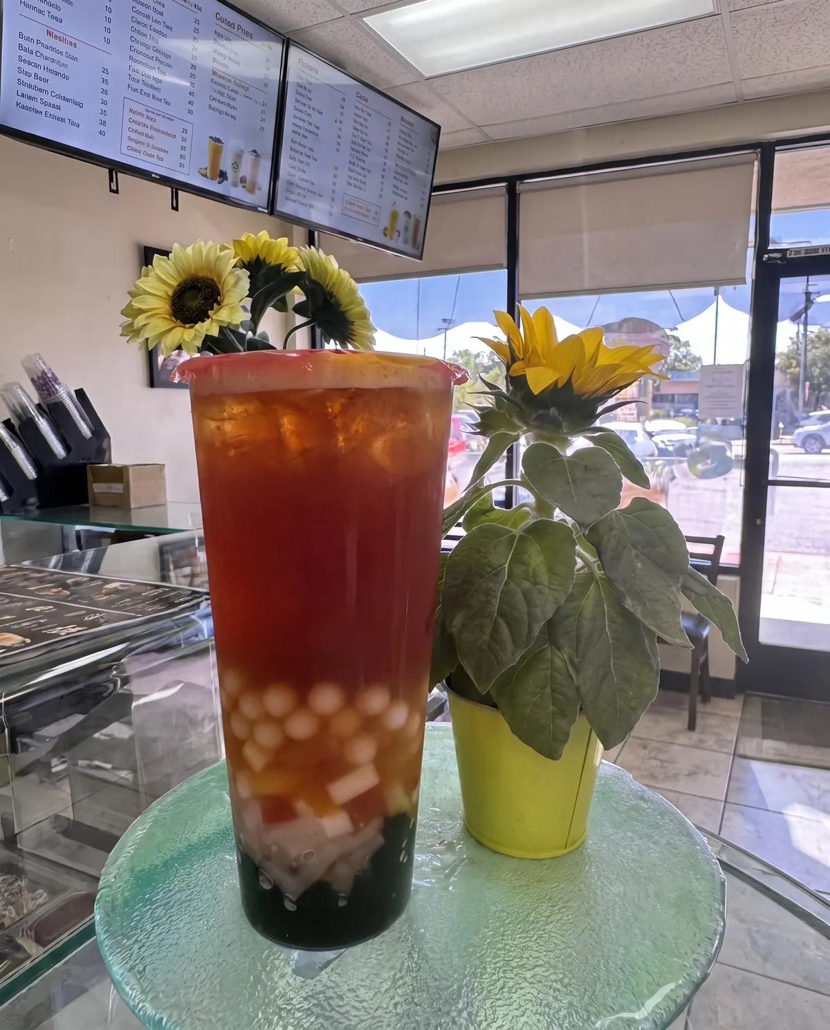 Iced fruit tea with crystal boba and jelly next to a potted sunflower