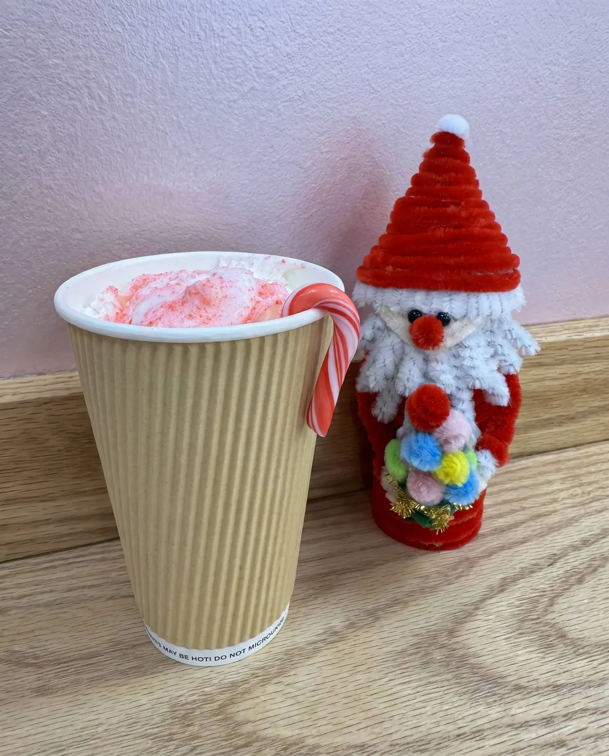 Hot drink with a candy cane next to a knitted Santa